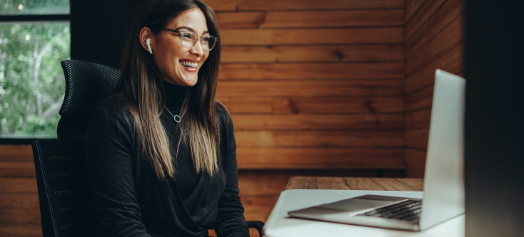 A person sits at a desk, smiling in front of a computer.